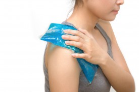 A woman is holding an ice pack on her shoulder.