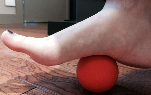 A foot rests on top of a small red ball to work on the plantar fasciiitis.