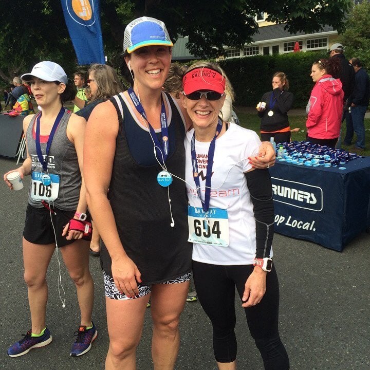 Sandy poses smiling with a friend, both in their racing gear, surrounded by the bay atmosphere of the half marathon.