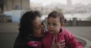 A woman in Vancouver, Joyce, holds her grand daughter outside while they play on playground beside the water on a grey, rainy day.