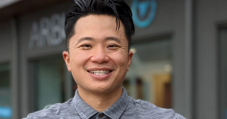 An asian man smiling in front of a building.