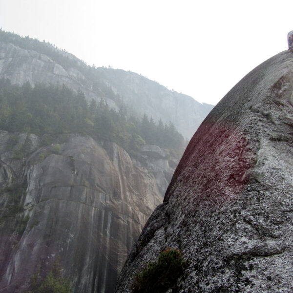 A rock climber works their way up a crack in the mountains, with their ropes dangling down toward the photographer.