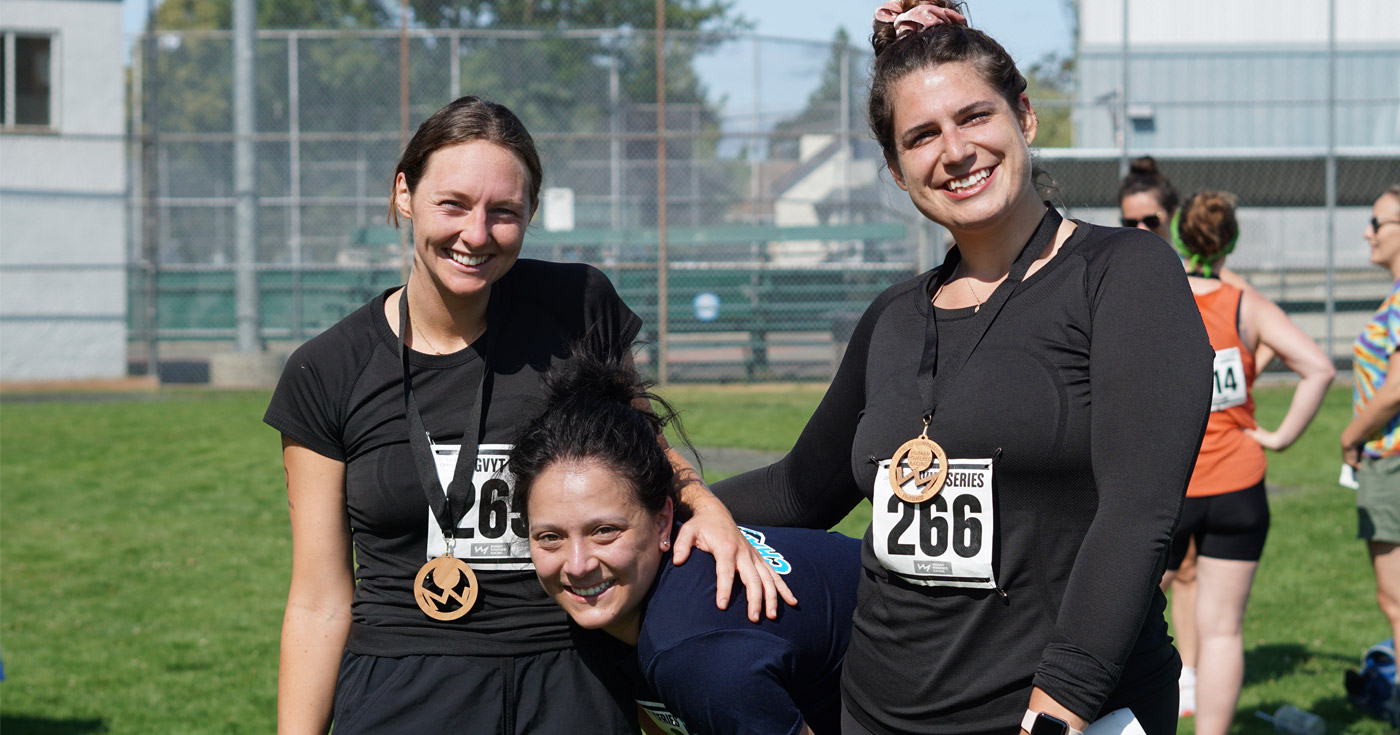 Three athletes recover at the end of the Triathlon of Compassion at Esquimalt Rec, smiling with their medals.