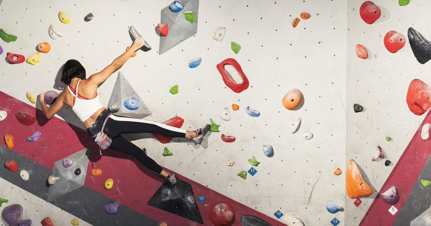 A woman practices a series of grips in an indoor bouldering climbing wall.