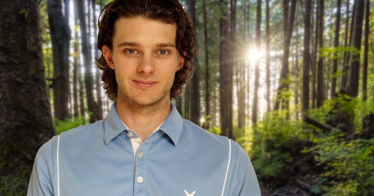 Joshua Grawbarger, Physiotherapist, stands smiling in a west coast rainforest, with the sun beaming through the trees.