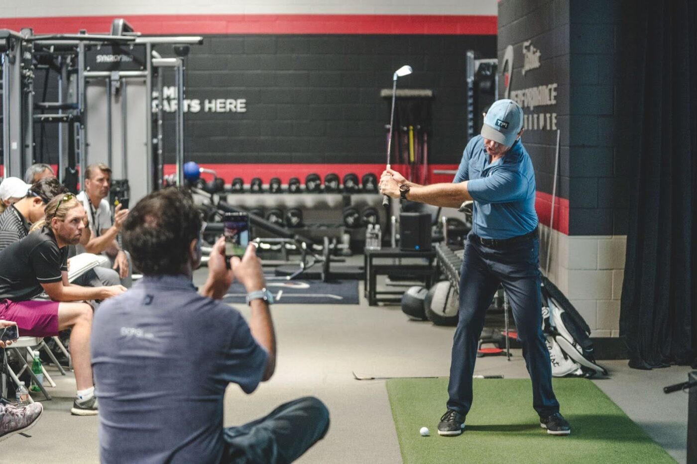 A participant takes a golf swing while physios capture the moment for analysis.