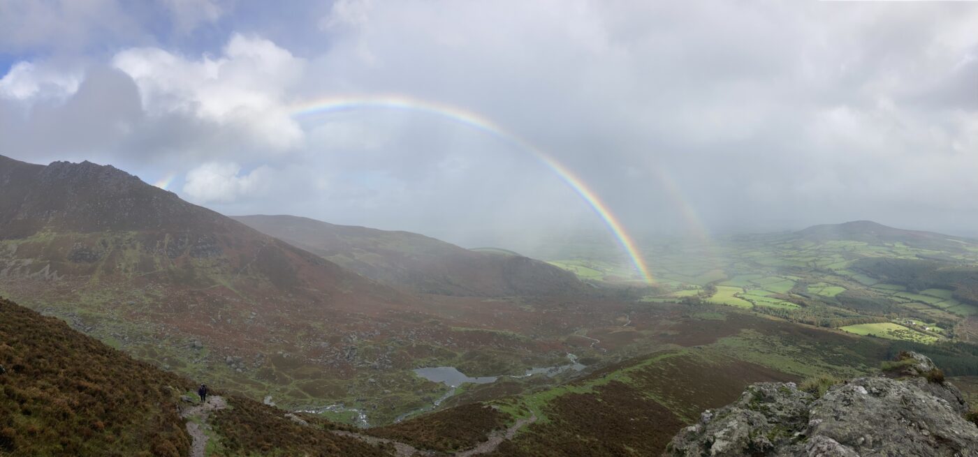 A view from the top of a mountain in Ireland, taken by Joseph Rector, overlooking rolling green hills, with clouds and a double rainbow in the distance.