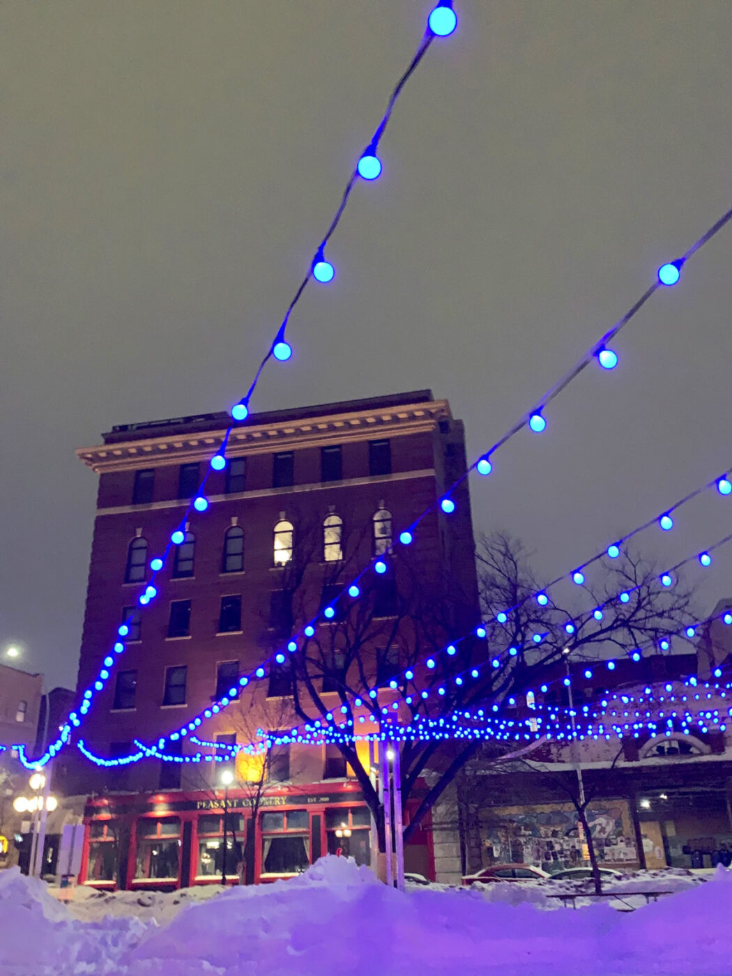 A beautiful city coffee shop looking very cozy in the snow and pretty blue lights.
