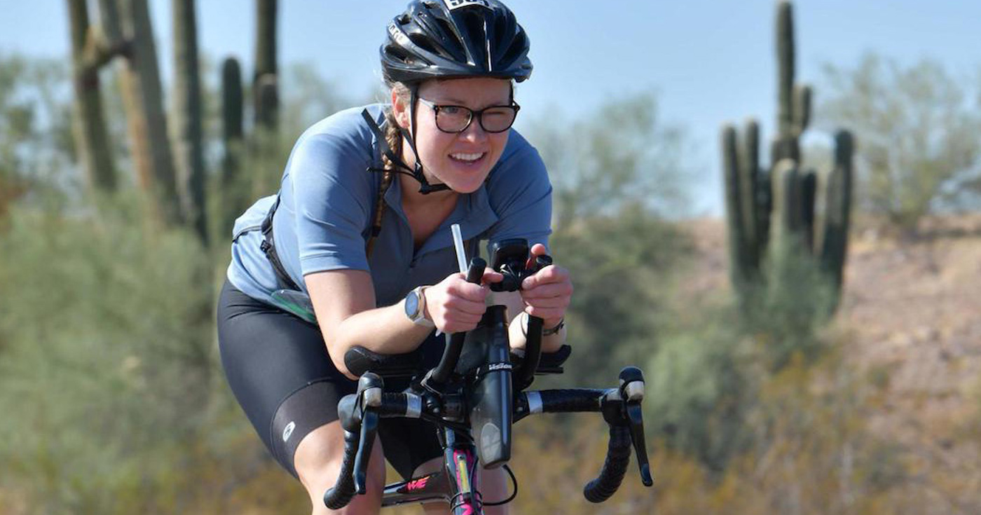 Madi Campbell bikes along a road in Phoenix, Arizona, with cactus in the background, while competing in the Ironman event.