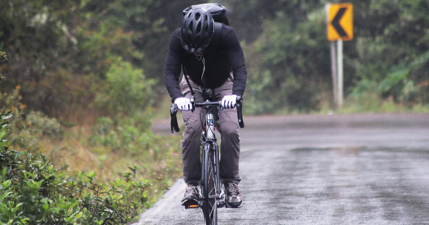 A commuter pushes through in the rain with gloves and wet pants.