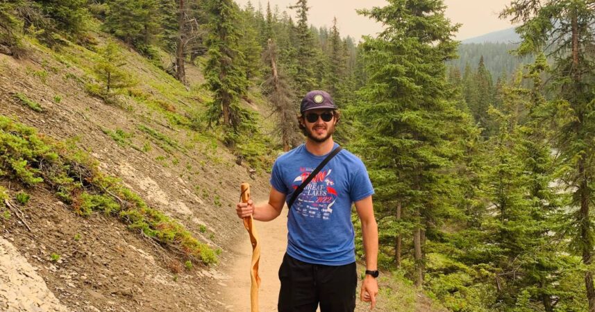 Josh Grawbarger hikes with a walking stick through a pine forest on Vancouver Island during a smoky summer.