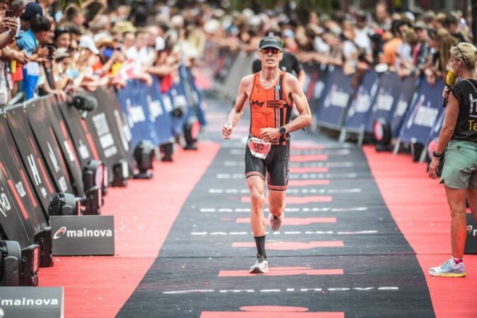 Mike Neill runs across the finish line of an Ironman event.