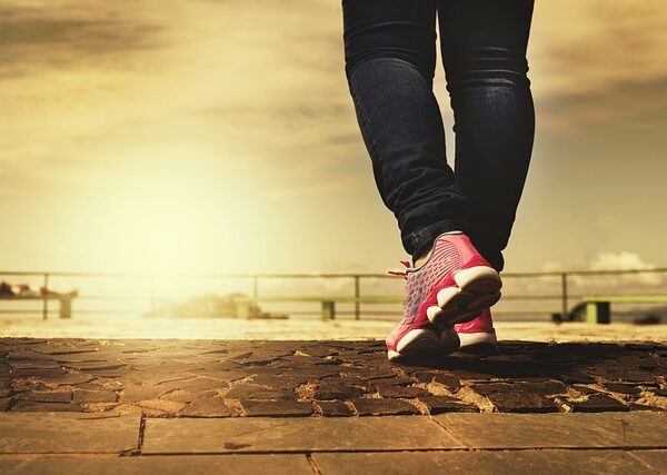 A person walking toward a sunset wearing pink sneakers, by Daniel-Reche.