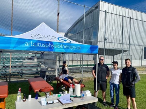 A group of people smiling beside the Arbutus Physio therapy tent on a sunny day.