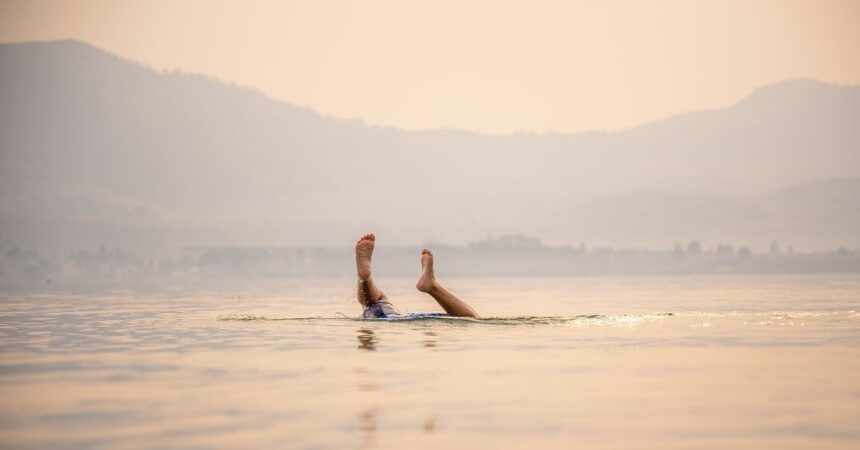 Someone's feet in the air as they dive under the water with misty mountains behind.