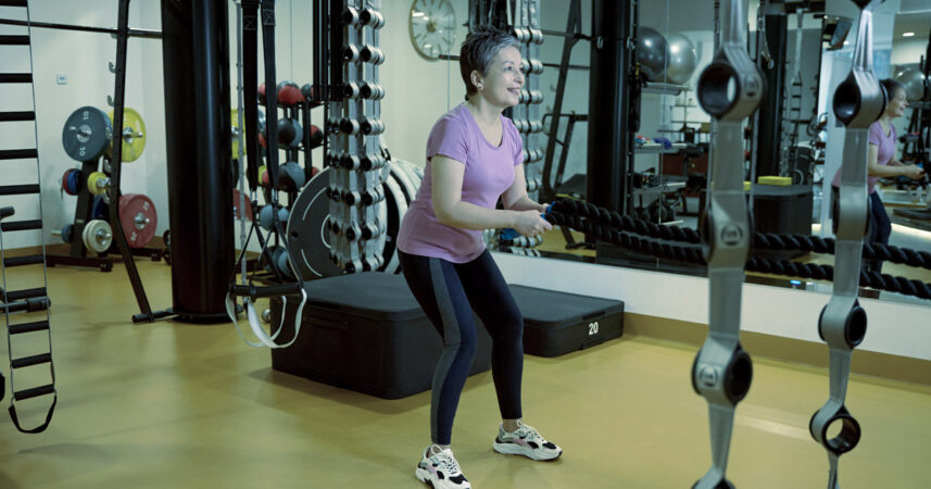 A woman does hip hinges in a gym, smiling, while looking in the mirror.
