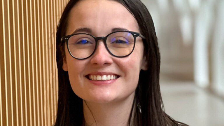 Hatty Skinner stands in the hallway at a university smiling through her epic glasses.