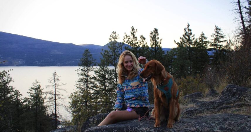 Jamie Kavanagh sits on a mountain with her dog Luna overlooking a lake.