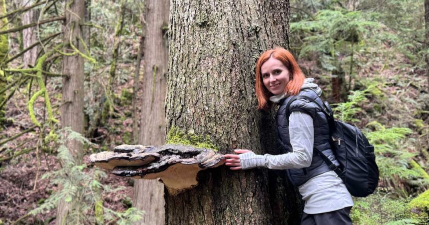 Oksana hugs an old growth tree with a large mushroom growing out of its side.