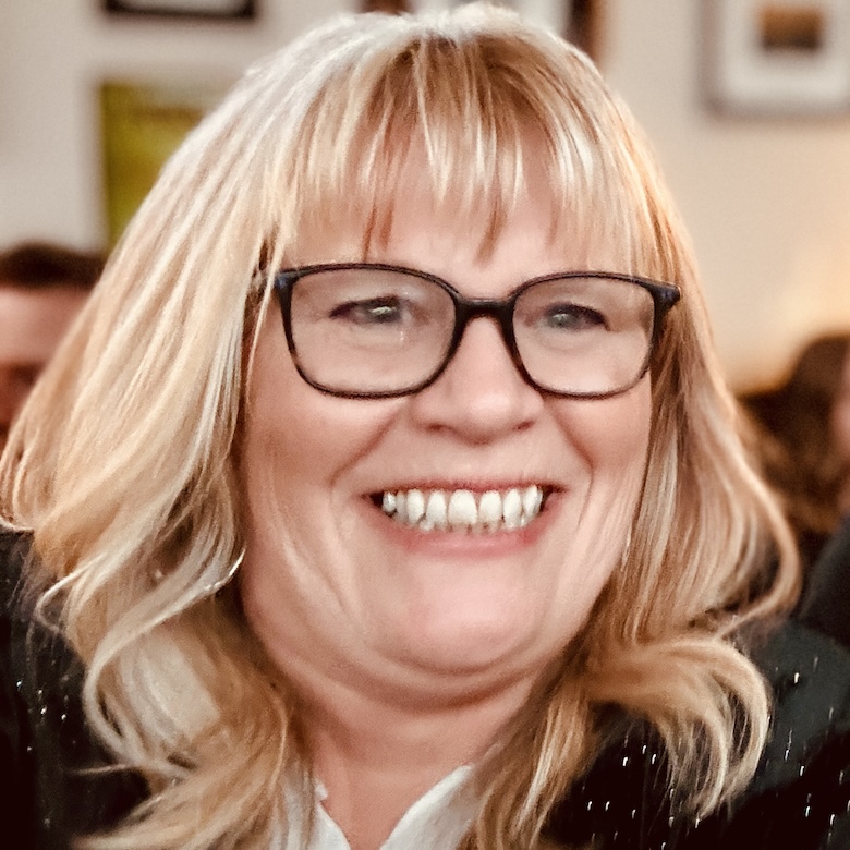 Richelle Osborne smiles wide, wearing dark framed glasses.