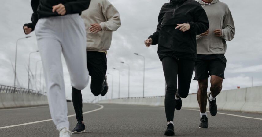 Four people run on a track, wearing various neutral toned clothing, with their faces cropped from the frame.