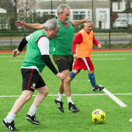 Aging adult men run around on the pitch looking happy and agile.
