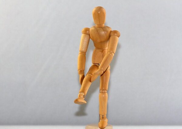 A wooden human figurine holds its knee.